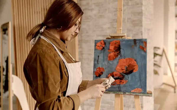 A painter working on a green canvas in a cluttered studio